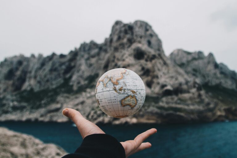 Hand weighing a small globe above the sea, symbolising a tour operator comparing Viator commission with Google Ads costs