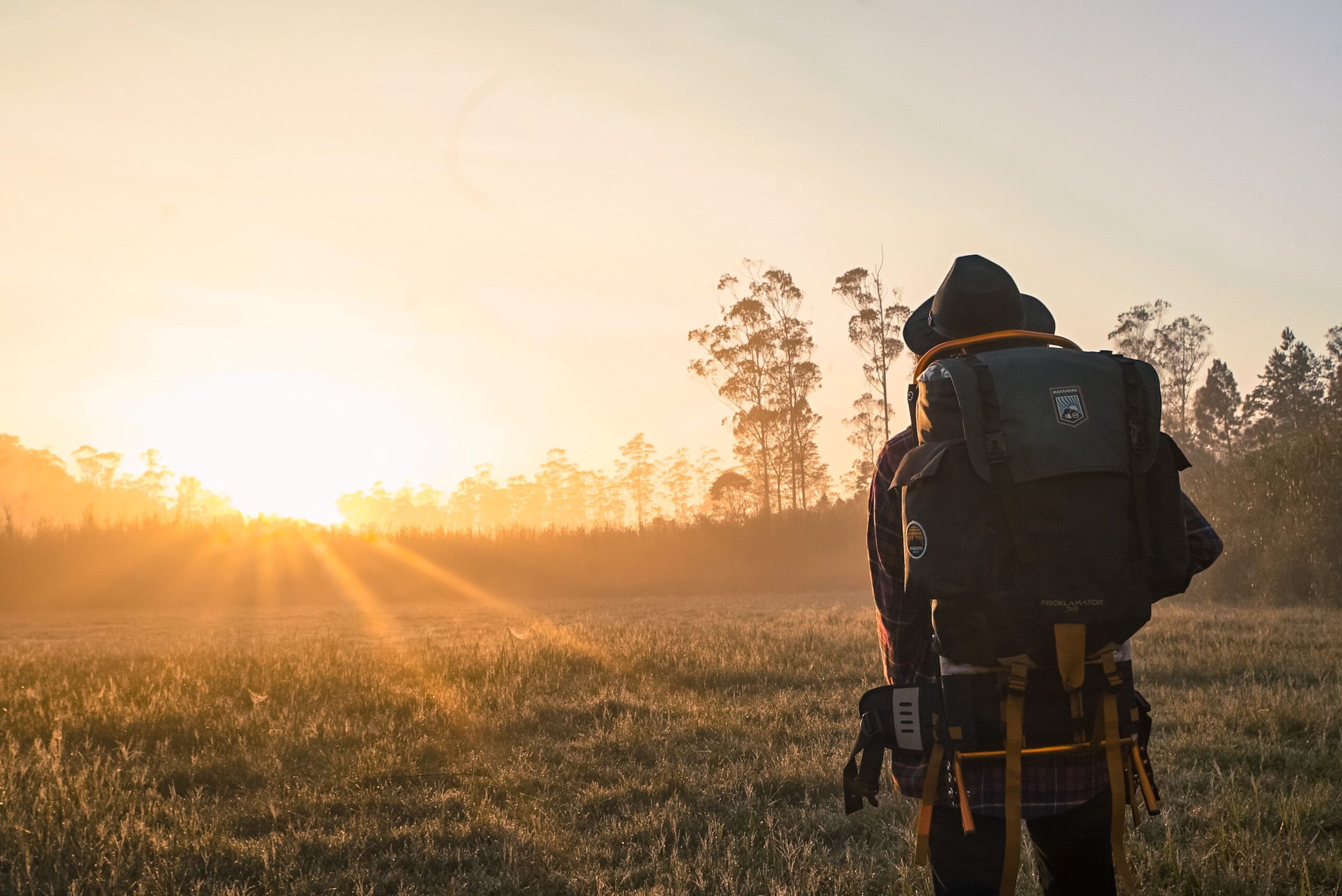 Traveller with a backpack watching the sunrise over a misty field
