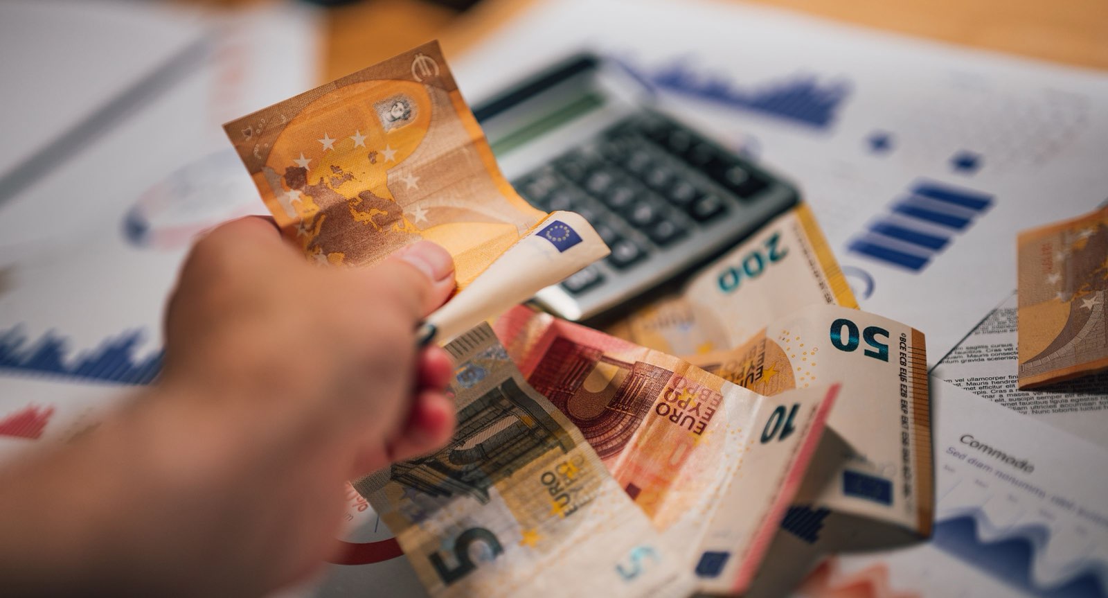 Counting euro notes beside a calculator and sales charts, representing OTA commission costs